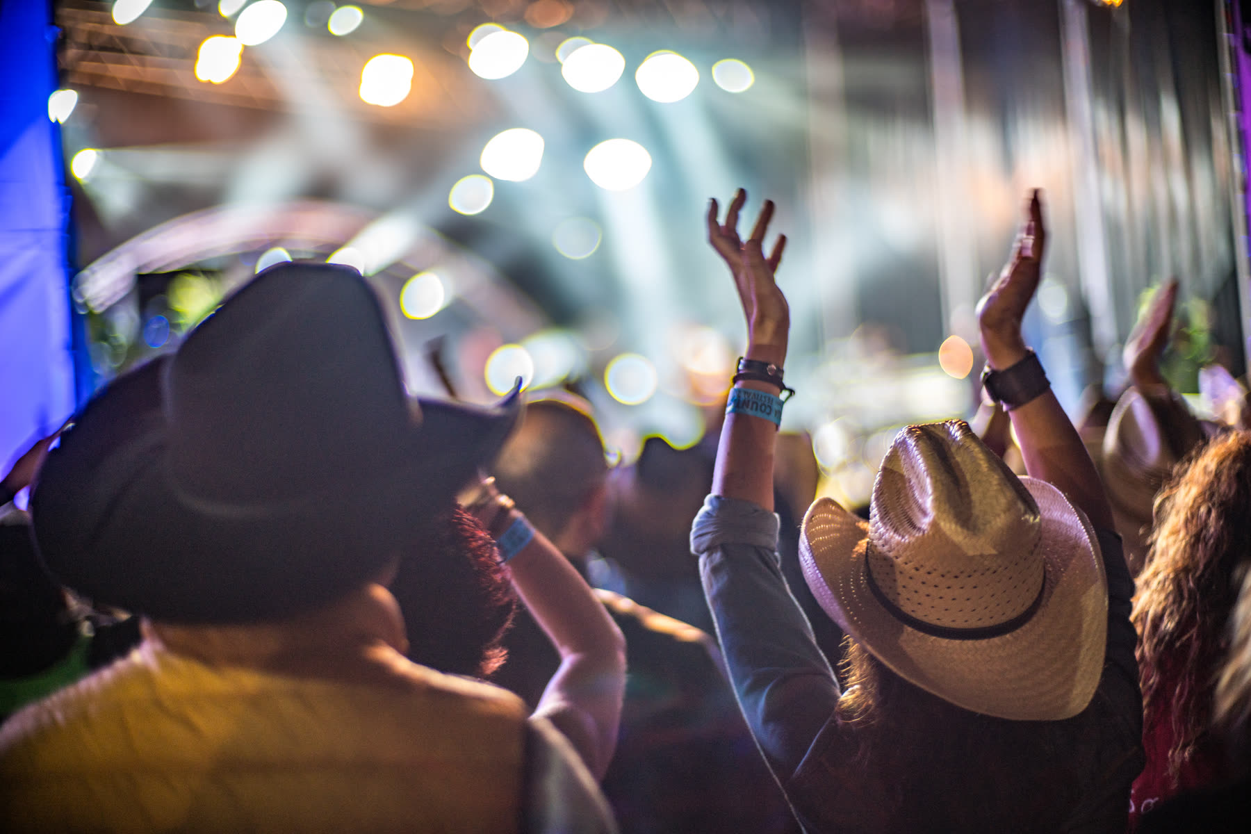 Country music festival crowd in cowboy hats with hands raised toward the stage