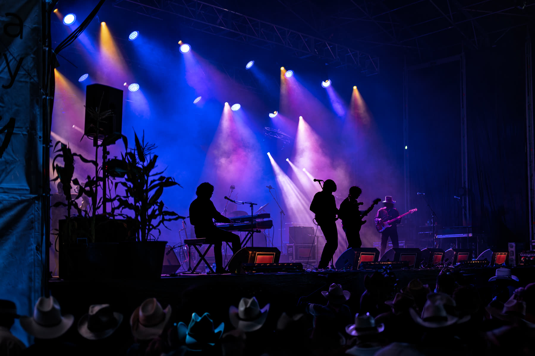 Country band silhouetted on a festival stage under blue and purple lights with cowboy hats in the crowd