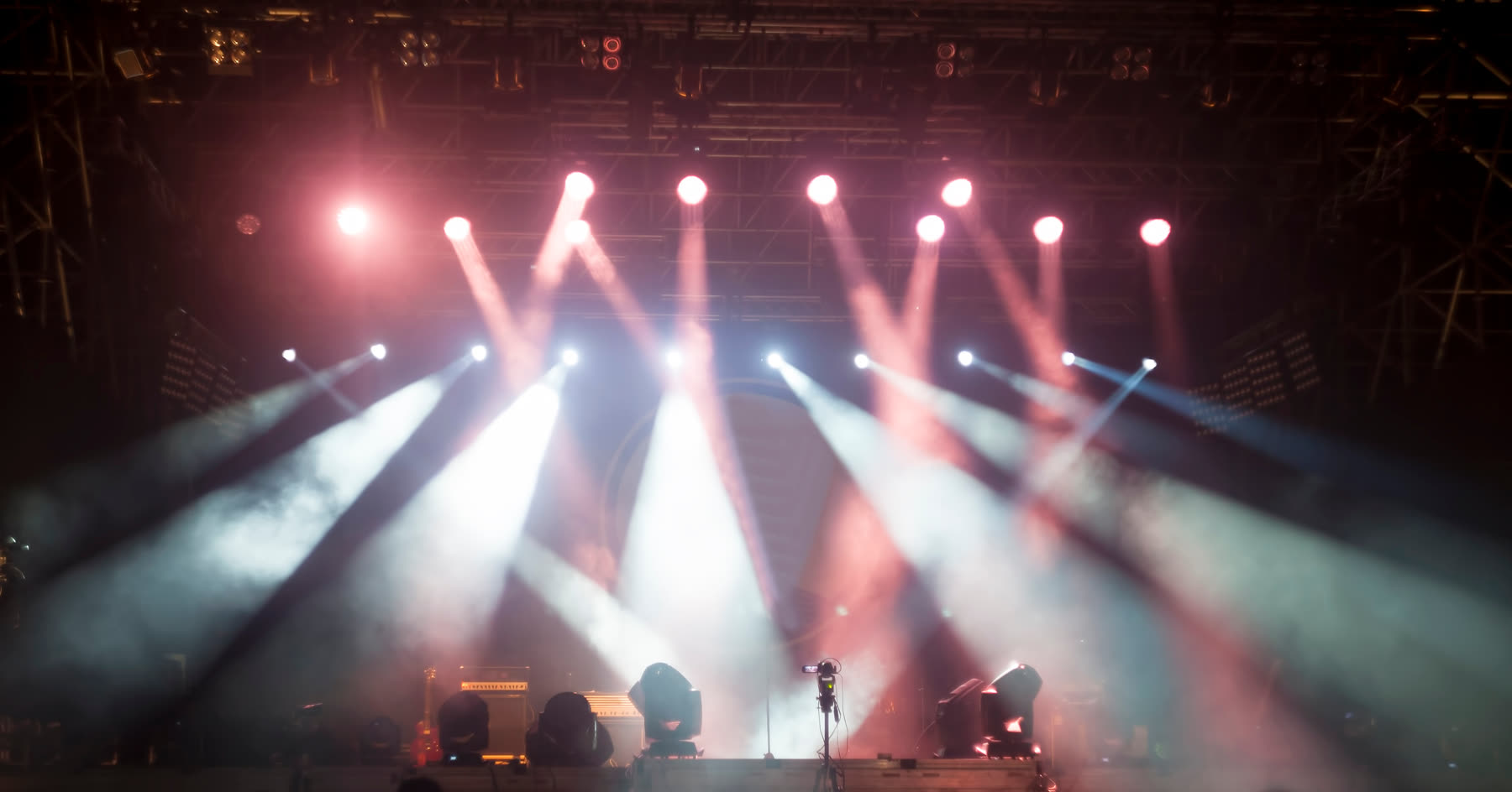 Concert stage lighting rig throwing blue and purple beams over an empty festival stage