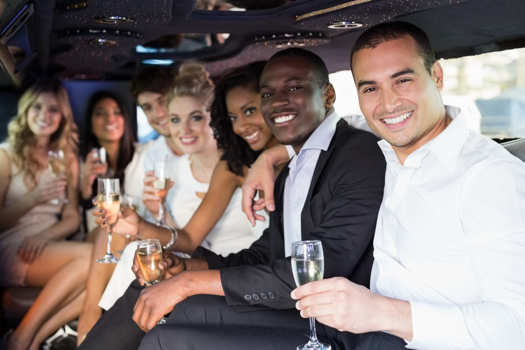 Formally dressed group seated along the perimeter bench of a stretch limousine cabin